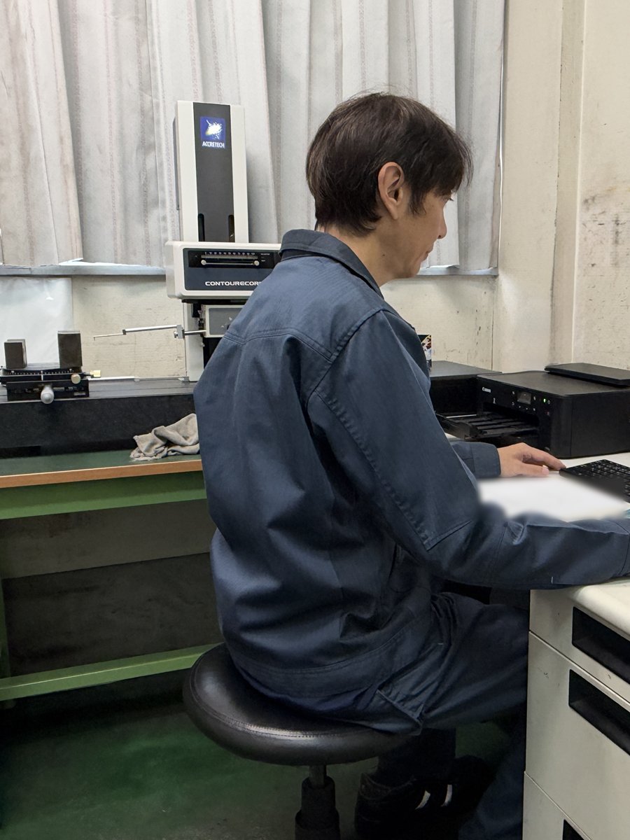 東京精密(ACCRETECH)の輪郭形状測定機 CONTOURECORD のそばで、パソコンの測定画面を確かめる作業者